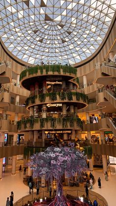 the inside of a shopping mall filled with lots of plants and people walking around it