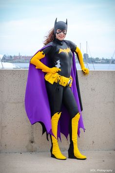 a woman dressed as batman standing next to a cement wall with her hands on her hips