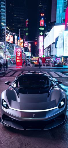 a silver sports car parked in the middle of a city street at night with neon lights