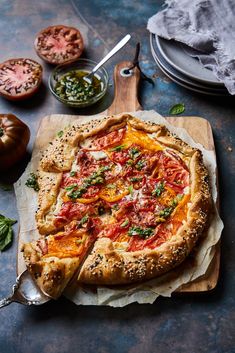 a pizza sitting on top of a wooden cutting board next to some tomatoes and other vegetables