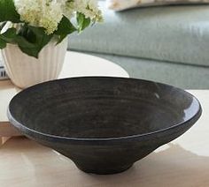 a black bowl sitting on top of a table next to a vase with white flowers