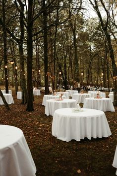 several tables are set up in the woods for an outdoor wedding reception with white linens