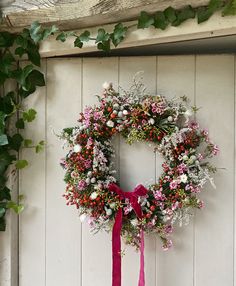 a wreath hanging on the side of a white door with pink ribbon and flowers around it