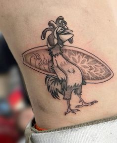 a rooster holding a surfboard tattoo on the back of a woman's leg