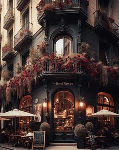 an old building with flowers on the balconies and tables under umbrellas outside