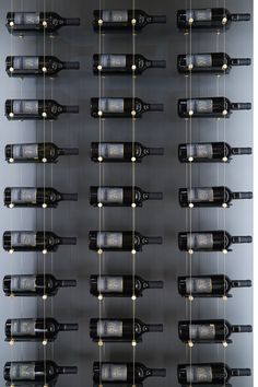 several rows of wine bottles are hanging from the ceiling in front of a metal wall