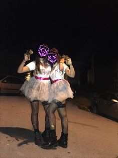 two girls dressed up in costumes standing on the street at night with their arms around each other