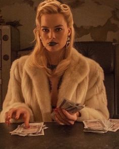 a woman sitting at a table with money in front of her and wearing a fur coat