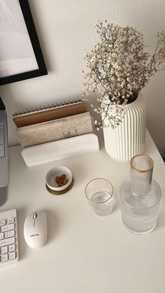 a white desk with a computer, keyboard and vase filled with baby's breath flowers