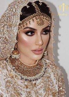 a woman in a white and gold bridal outfit with jewelry on her head, wearing a veil