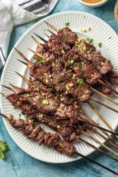 skewered steaks on a white plate with chopsticks and dipping sauce