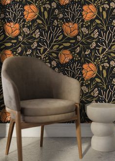 a chair sitting in front of a wallpaper with orange flowers and leaves on it