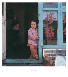 a young child standing in the doorway of a building with chinese characters on it's windows