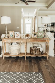 a wooden table topped with pictures and baskets next to a lamp on top of a hard wood floor