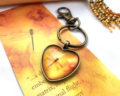 a heart shaped keychain with a dragonfly on it sitting next to a book