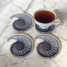 four blue and white plates with spiral designs next to a cup of tea