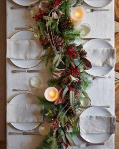 the table is set with white plates, silverware and greenery as well as candles