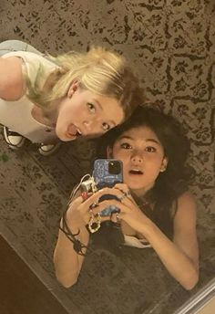 two young women taking a selfie in front of a mirror with their cell phone