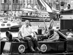 black and white photograph of an older man sitting on a boat in a harbor with other boats