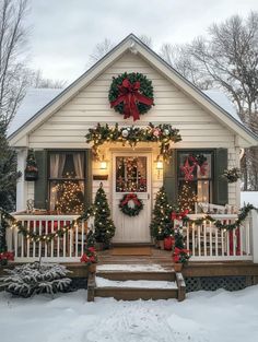 a white house decorated for christmas with wreaths and lights on the front porch, covered in snow