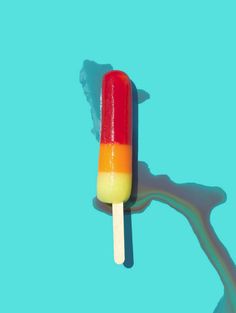 an orange and yellow popsicle sitting on top of a blue surface with the shadow of a tree behind it