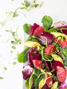 a white plate topped with greens and sliced up beets next to other food items