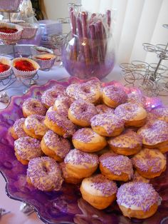 a plate full of purple sprinkled donuts on a table with other desserts