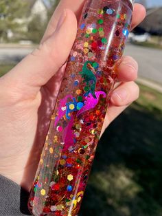 a hand holding a glass bottle filled with colorful confetti