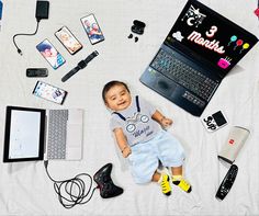 a baby laying on top of a bed next to electronics