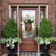 two black planters with white flowers are on the front steps of a brick house