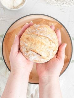 two hands holding a loaf of bread in a bowl