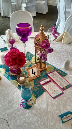 the table is decorated with pink roses and purple glassware for guests to sit at