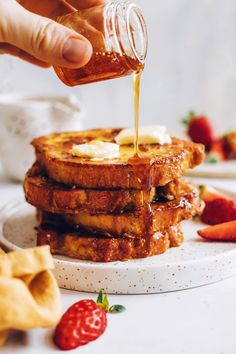 a person pouring syrup on some french toast with strawberries and crackers in the background