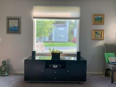 a living room with a large window and a tv on top of a dresser next to a chair