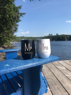 two wine glasses sitting on top of a blue bench next to the water with trees in the background