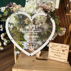 a heart shaped mirror sitting on top of a wooden table next to a sign and flowers