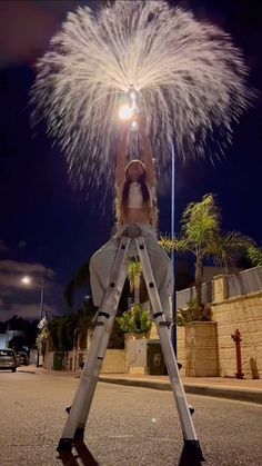 a woman standing on top of a ladder holding a light up firework in the air