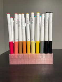 several pens are lined up next to each other on a wooden holder with pink base