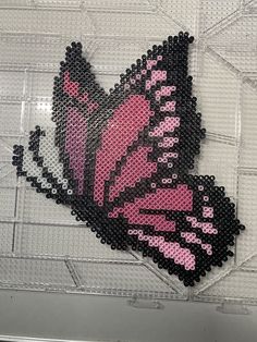 a pink and black beaded butterfly sitting on top of a white wall next to a window