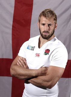 a man with his arms crossed standing in front of a flag and wearing a polo shirt