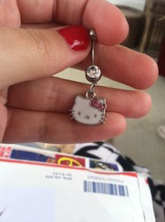 a person holding a hello kitty belly ring in their left hand and wearing a red manicure