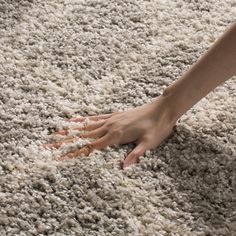 a person's hand reaching for something on a carpet that is white and gray