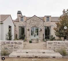 a stone house with two doors and windows on the front, surrounded by brick walls