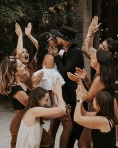 a group of people standing around each other with their arms in the air and one person wearing a hat