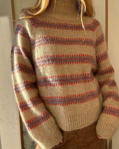 a woman standing in front of a door wearing a brown sweater and tan cord skirt