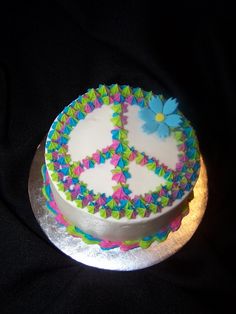 a peace sign cake is decorated with colorful icing on a silver platter and black background