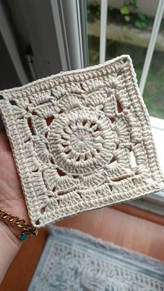 a hand holding a crocheted square in front of a window with a chain around it