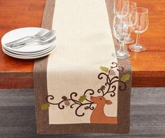 a table runner with a deer design on it and wine glasses next to the place setting