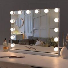 a vanity mirror with lights on top of it and a vase in the foreground