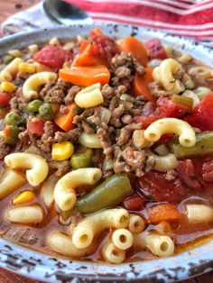 a white bowl filled with pasta and vegetables on top of a wooden table next to a spoon